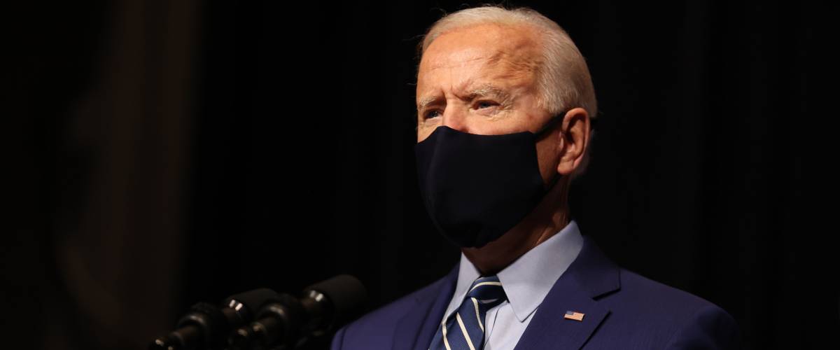 President Joe Biden speaks at a podium wearing a mask