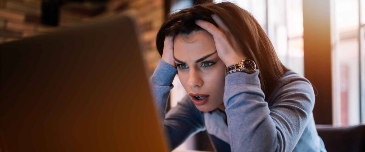 Frustrated worried young woman looks at laptop upset by bad news.