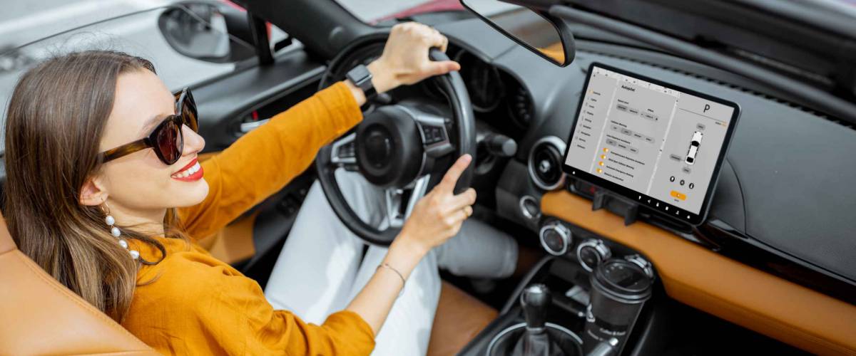 Young and cheerful woman driving sports car with a digital touchscreen with launched controlling program on the front dashboard