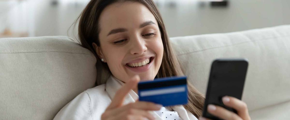 Happy young woman smiling while holding phone and bank card