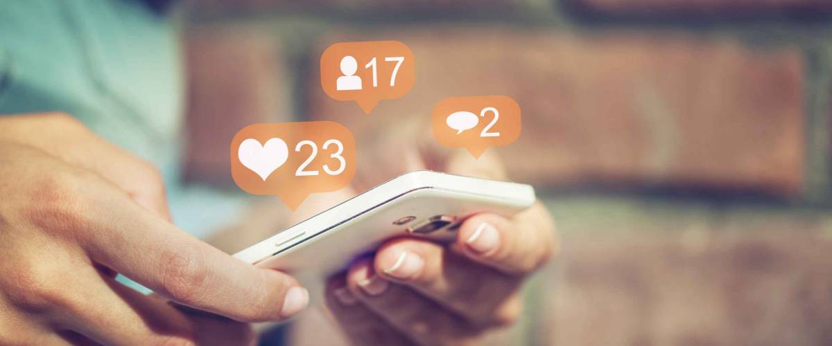 Close up of person holding smartphone, bubbles of social media likes, shares and comments above it