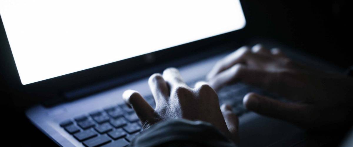 Hooded computer hacker stealing information with laptop