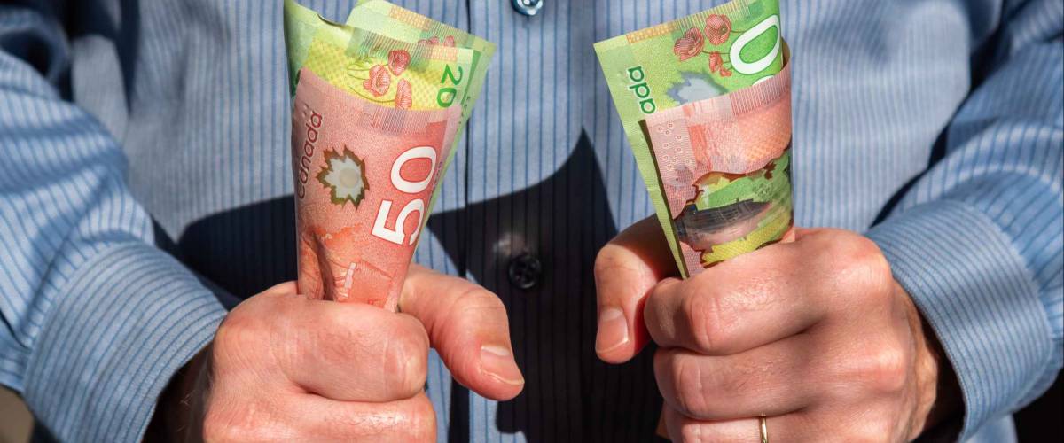 Man tightly holding Canadian twenty and fifty dollar bills in both hands