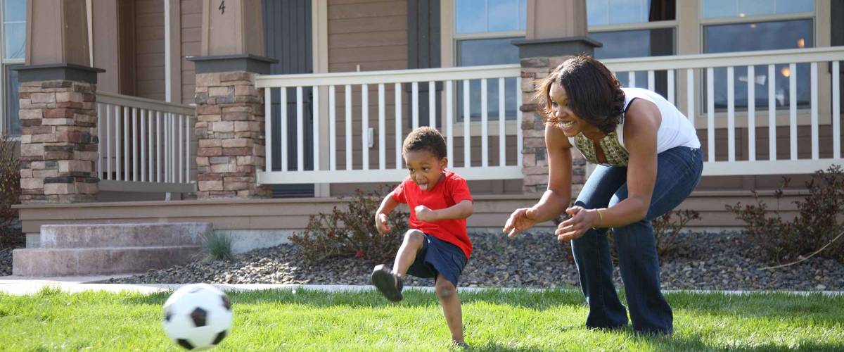 Mother and son in front yard playing with soccer ball