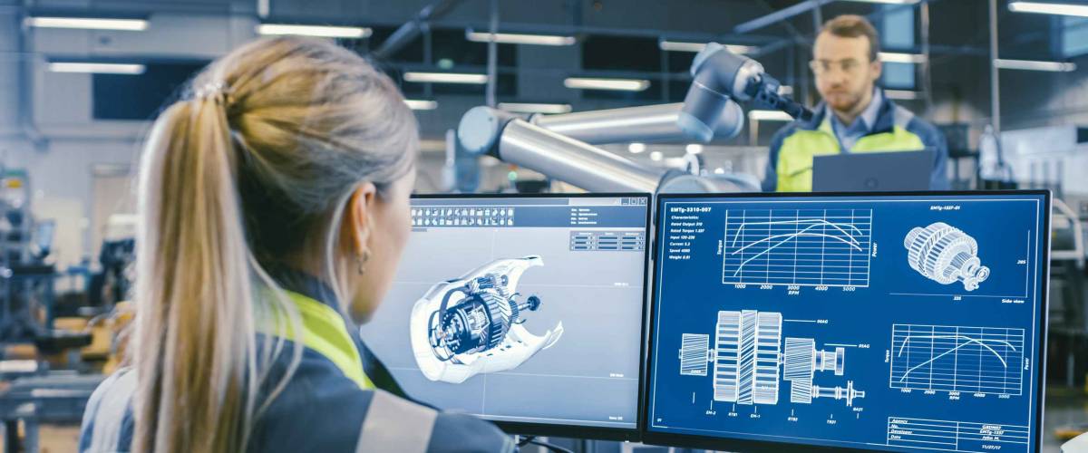 At the Factory: Female Mechanical Engineer Designs 3D Engine on Her Personal Computer. In the Background Male Automation Engineer who Uses Laptop for Programming Robotic Arm.