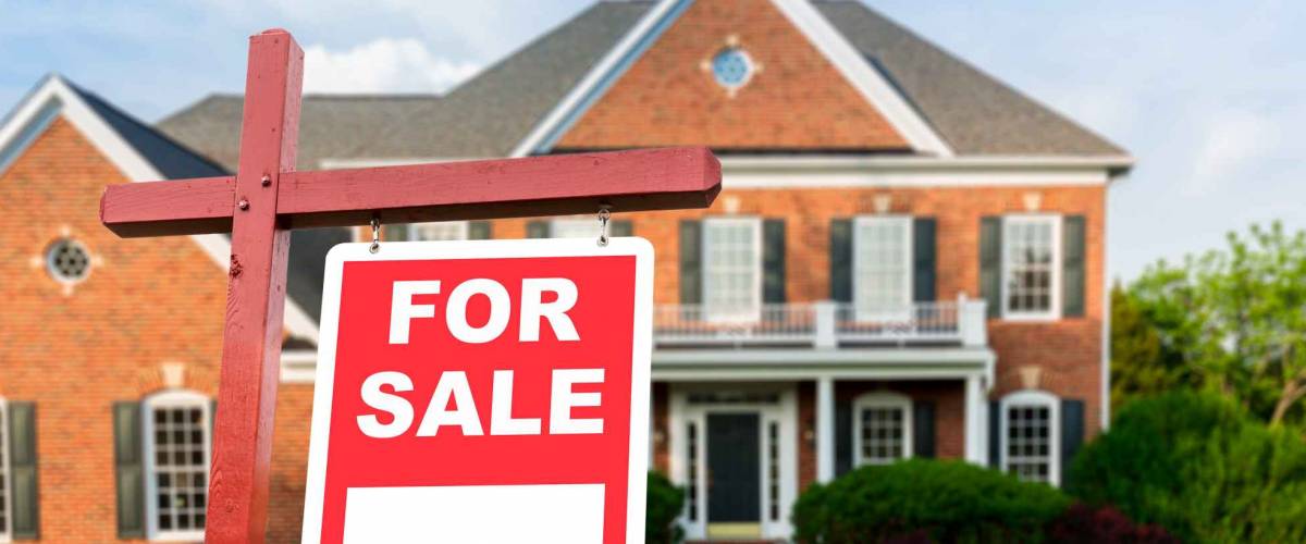 For Sale realtor sign in front of large brick single family house in expansive grass yard for real estate opportunity