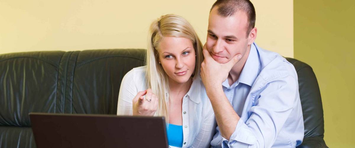 Portrait of young couple browsing the net on laptop at home.