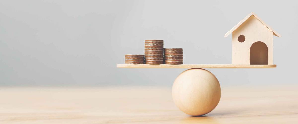 Wooden home and money coins stack on wood scale. Property investment and house mortgage financial real estate concept