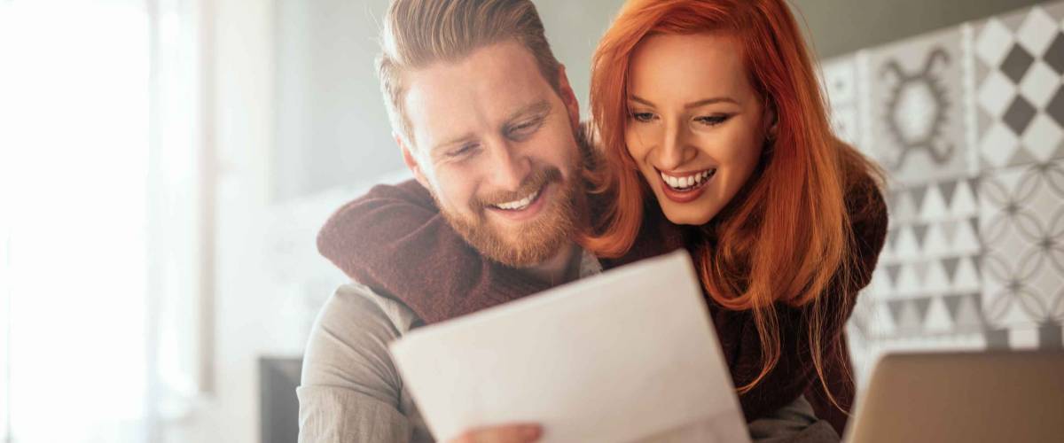 Photo of a positive young couple embracing and calculating the bills at home.
