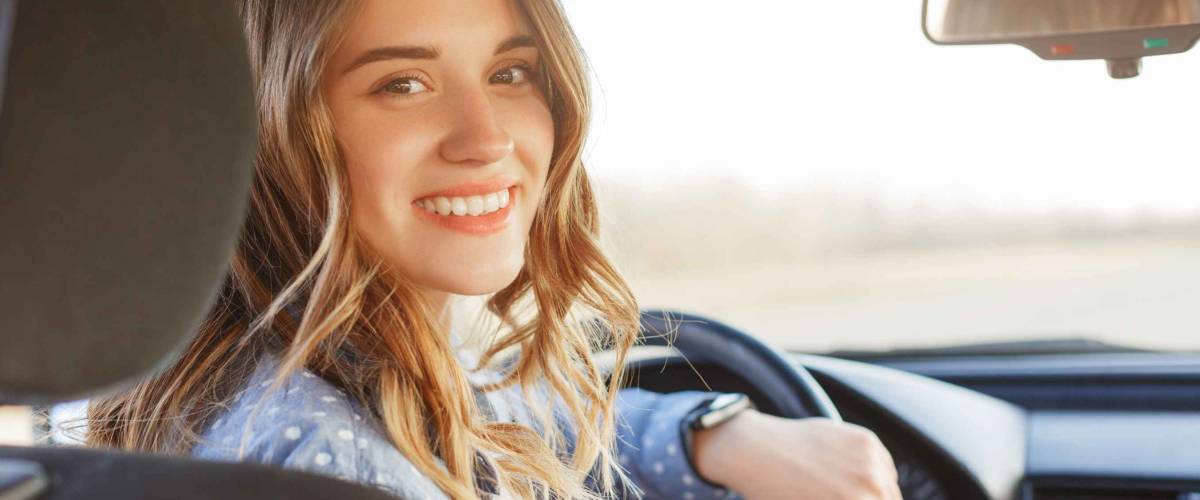 Young woman in the driver's seat, turned around and smiling into backseat