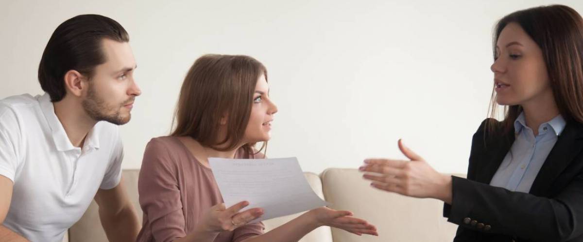 Young indignant woman sitting next to man indoors holding documents arguing with female agent or manager after detecting mortgage risk-free fraud, unfair contract terms, insurance scam