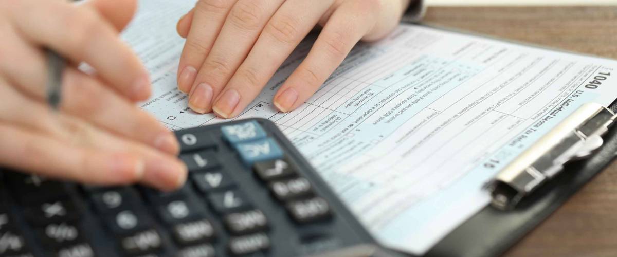 Female hand holding a pen and using calculator while filling in the individual income tax return, close up