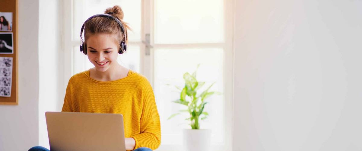 A young female student sitting at the table, using headphones when studying.