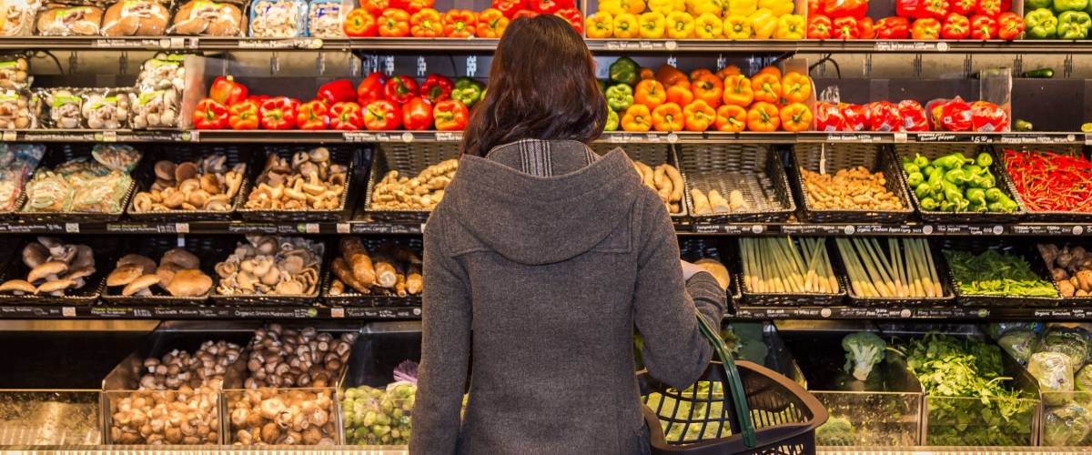 Woman standing in front of a row of produce in a grocery store.