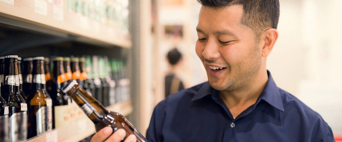 Handsome Young Asian man happy selecting a beer from supermarket.