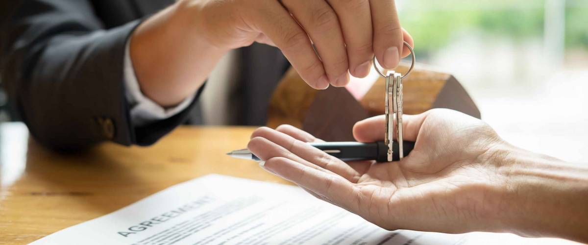 real estate agent holding house key to his client after signing contract agreement in office,concept for real estate, moving home or renting property