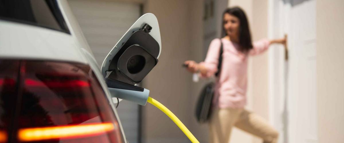 Close up of a electric car charger with female silhouette in the background, entering the home door and locking car