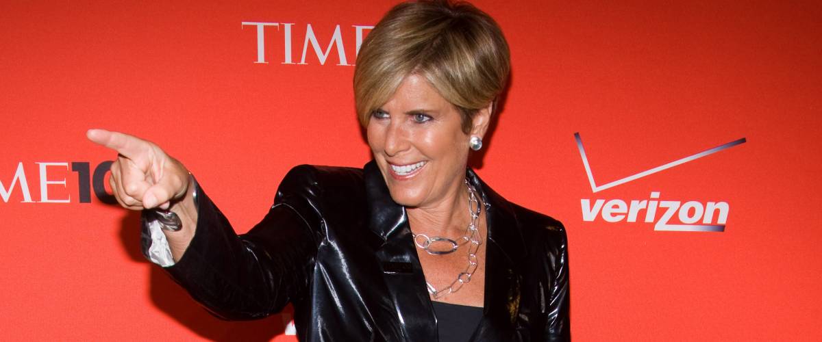 Suze Orman in front of a step-and-repeat at an event, smiling and pointing