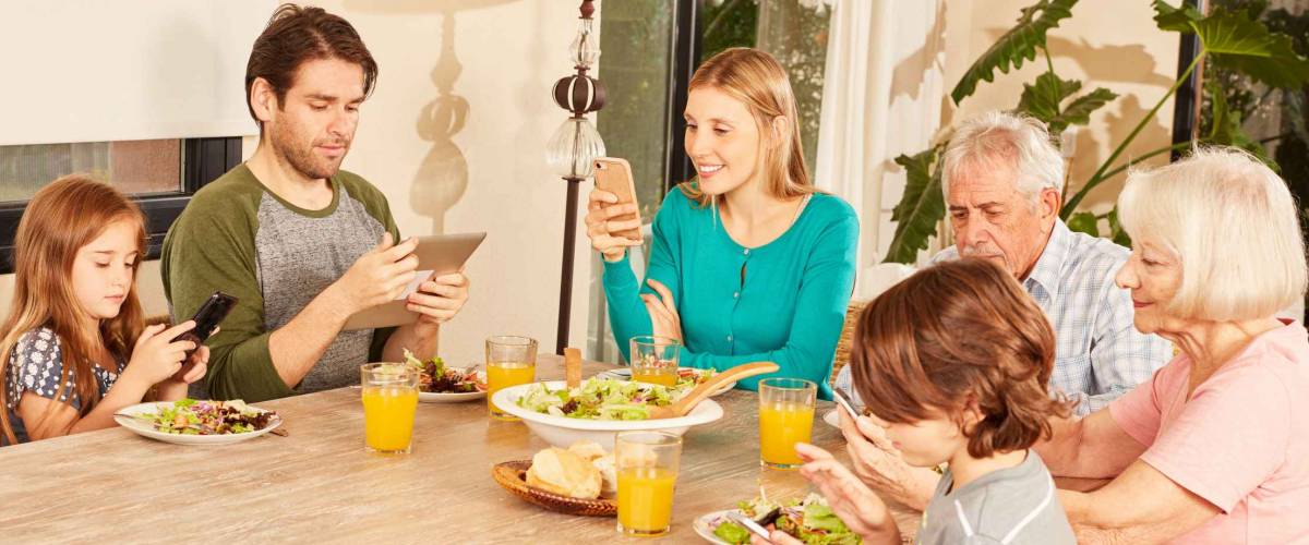 Extended family with three generations sitting at the dining table with tablet and smartphones