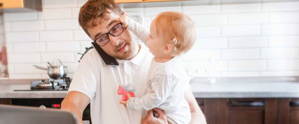 Handsome young man working at home with a laptop with a baby on his hands. Stay home concept. Home office with kids.