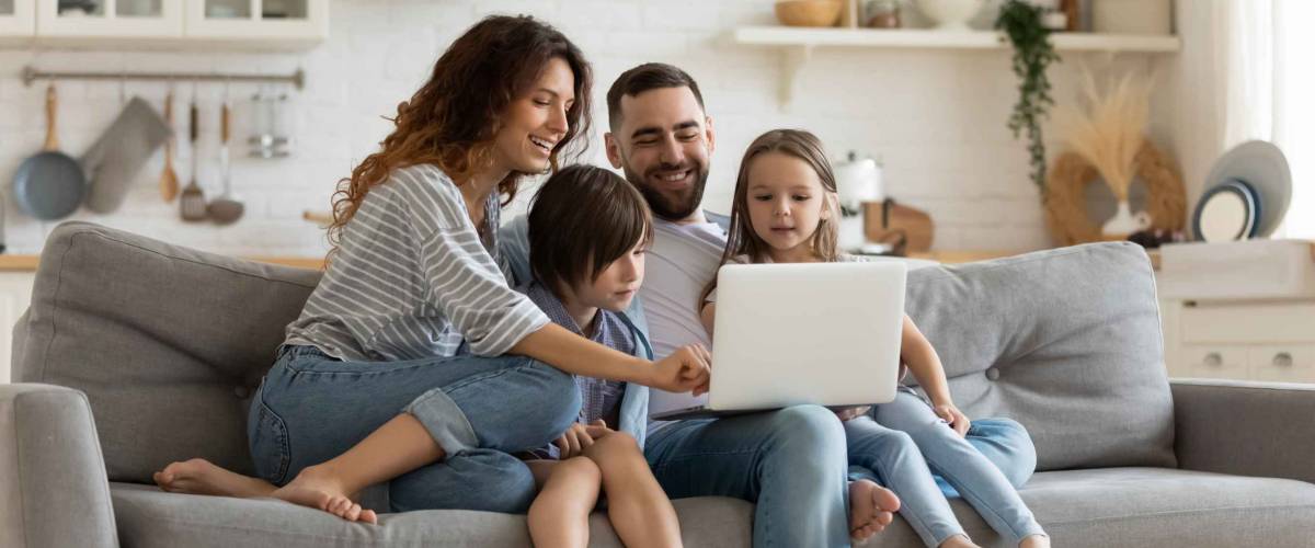 Happy young family with little kids sit on sofa in kitchen looking at laptop