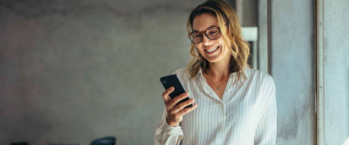 Smiling businesswoman using phone in office. Small business entrepreneur looking at her mobile phone and smiling.