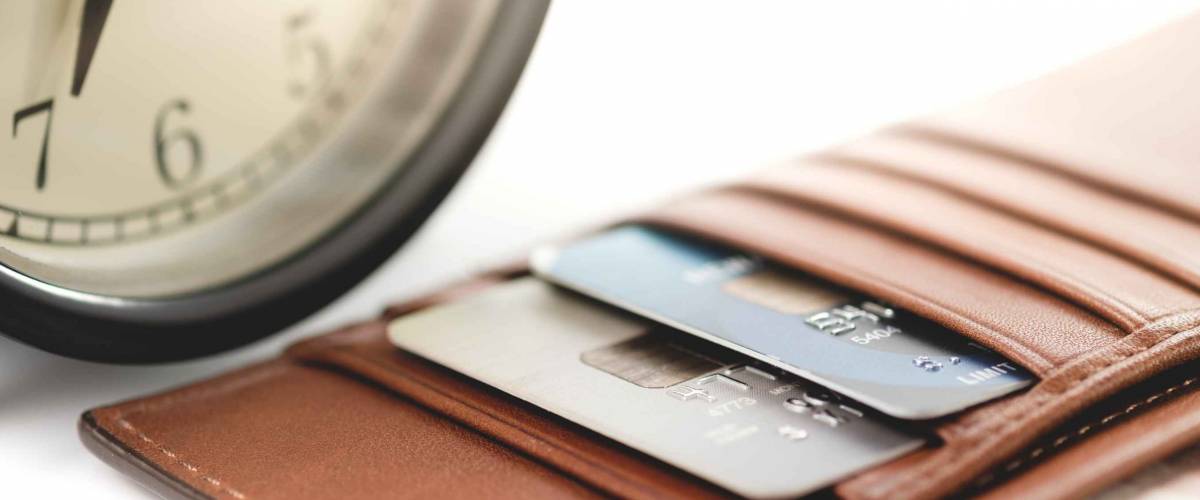 Credit cards in brown wallet with black analog clock on white background