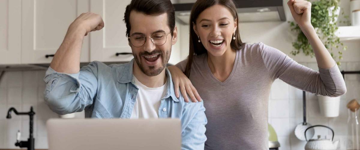 Euphoric young family couple looking at laptop screen, celebrating online lottery win notification.