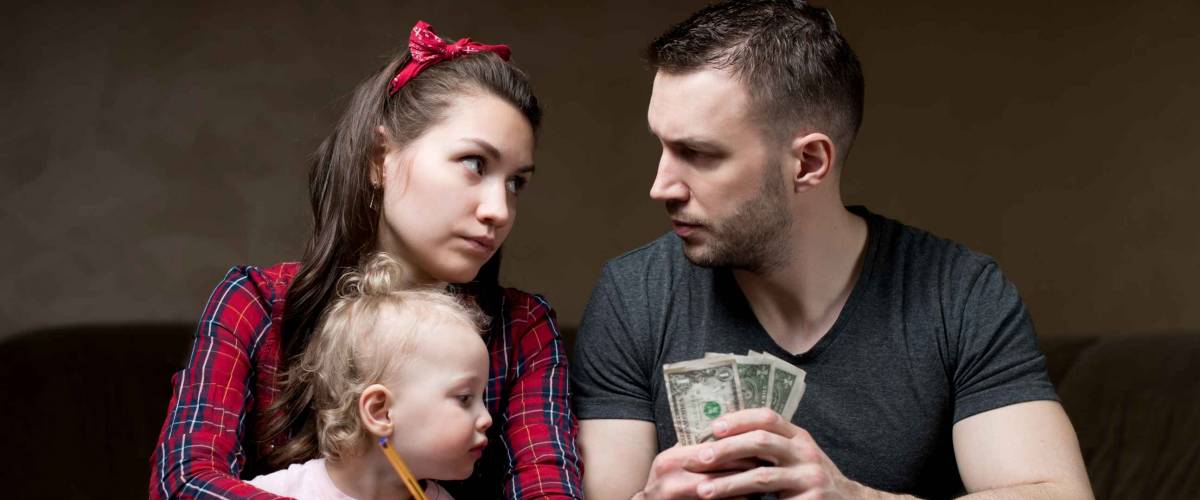 Counting family money. Husband and wife look at each other seriously, a little daughter sits on his wife s lap. Financial difficulties in a young family, crisis, lack of money