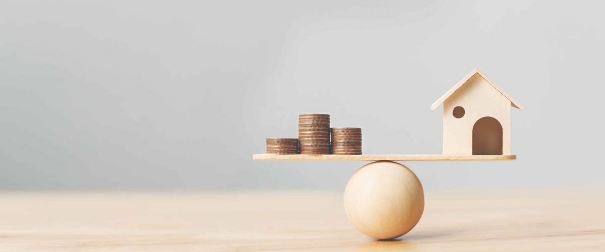Wooden home and money coins stack on wood scale. Property investment and house mortgage financial real estate concept