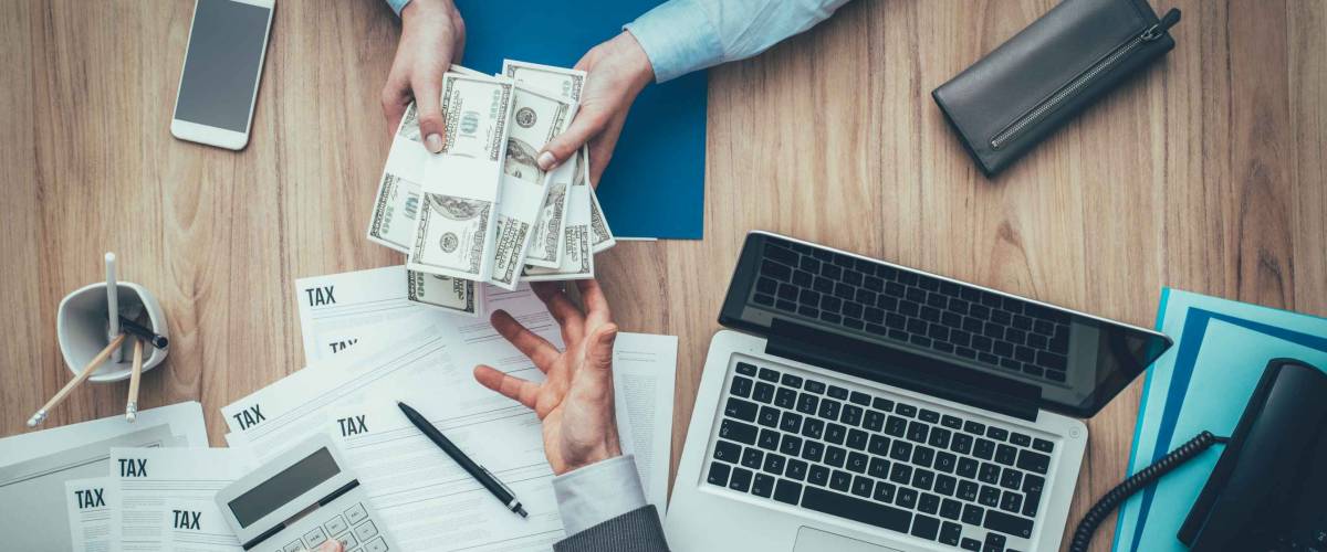 Business woman giving packs of dollars to her accountant and paying taxes, he is examining tax forms and calculating expenses