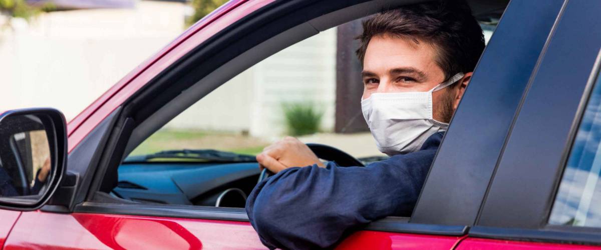Young male driver inside car with protective face mask