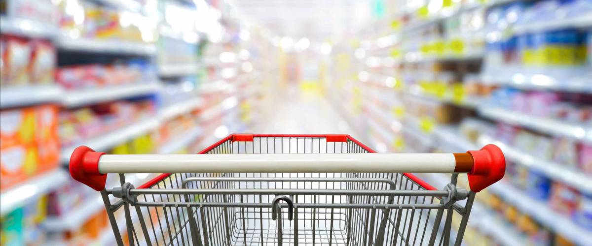 Supermarket aisle with empty red shopping cart.