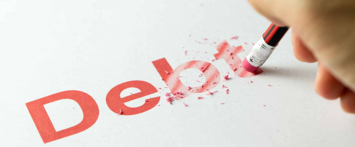 Close up of red pencil erasing the word debt on paper