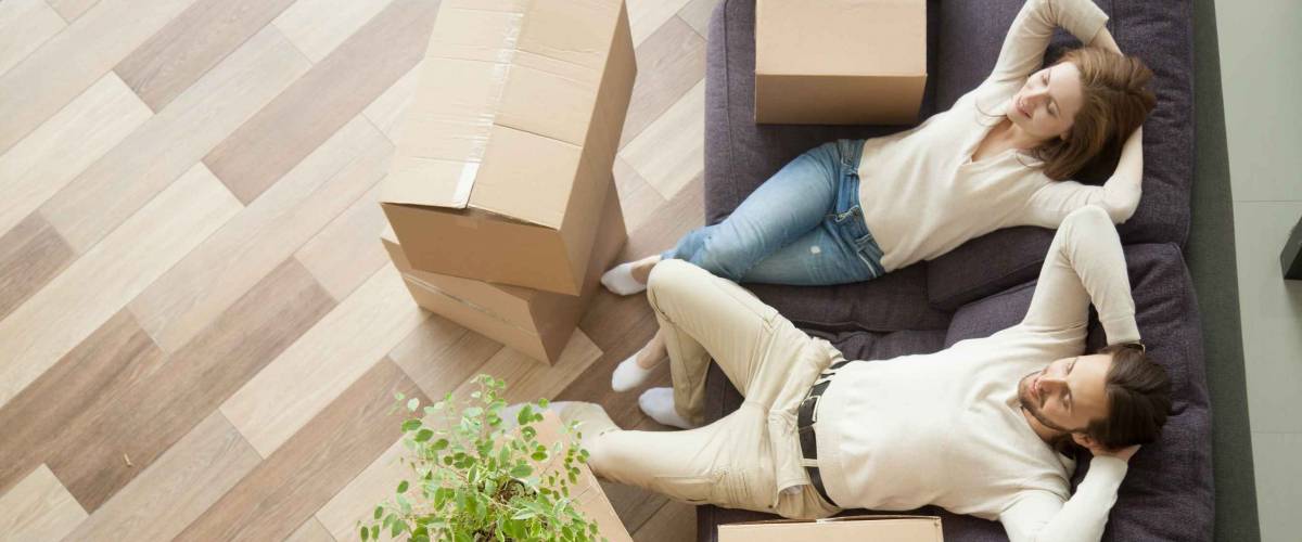 Couple resting on couch after moving in, man and woman relaxing on sofa just moved into apartment