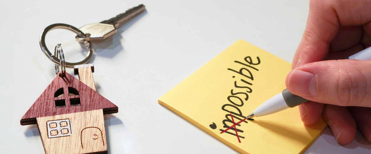 Yellow note with wording impossible with pen cross out on first 2 alphabets and house key chain , possible to own a dream home concept ,selective focus