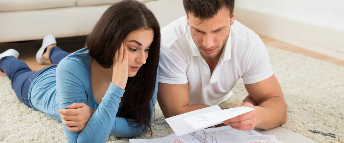 Worried Young Couple Lying On Carpet Looking at Their Bills At Home