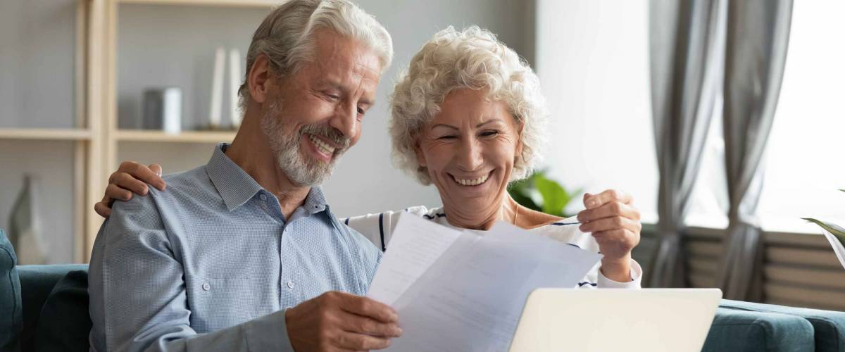Happy middle aged family couple sitting on couch, looking through papers.