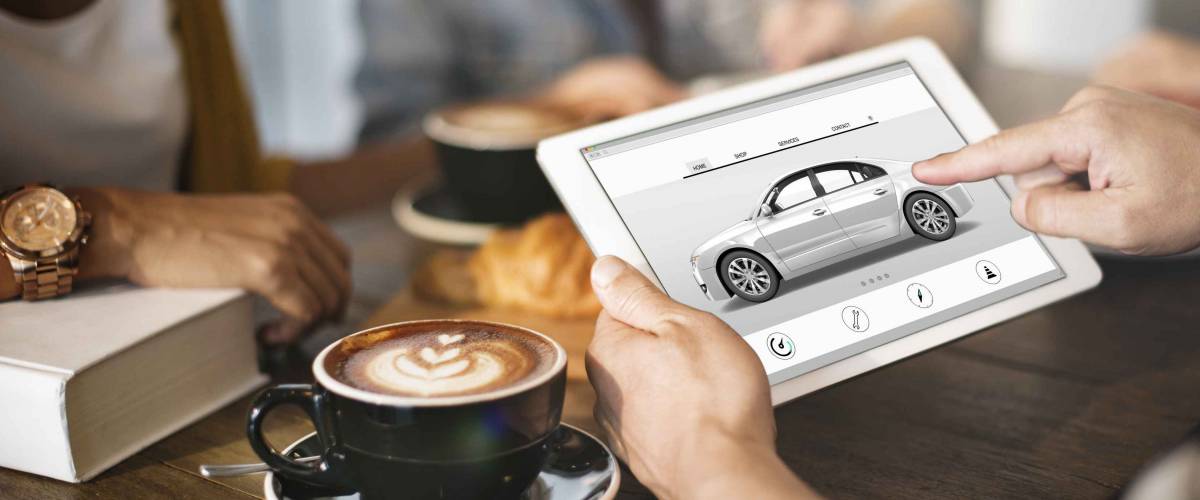 Person holding up tablet, looking at picture of car over table with latte and croissant on it