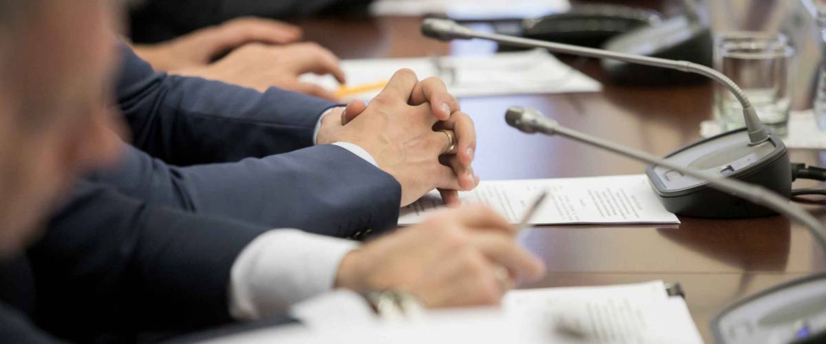 Close up of hands at table, crossed over pile of papers