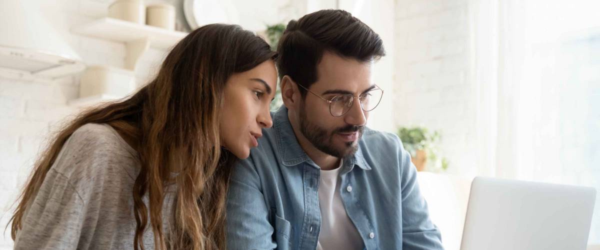 Focused young couple looking at laptop at kitchen table