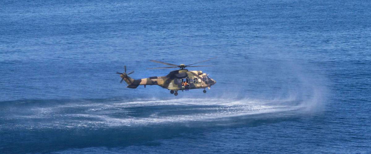 Army Military Rescue helicopter performing training rescue operation at sea. Helicopter drops divers soldiers during search and rescue operation.