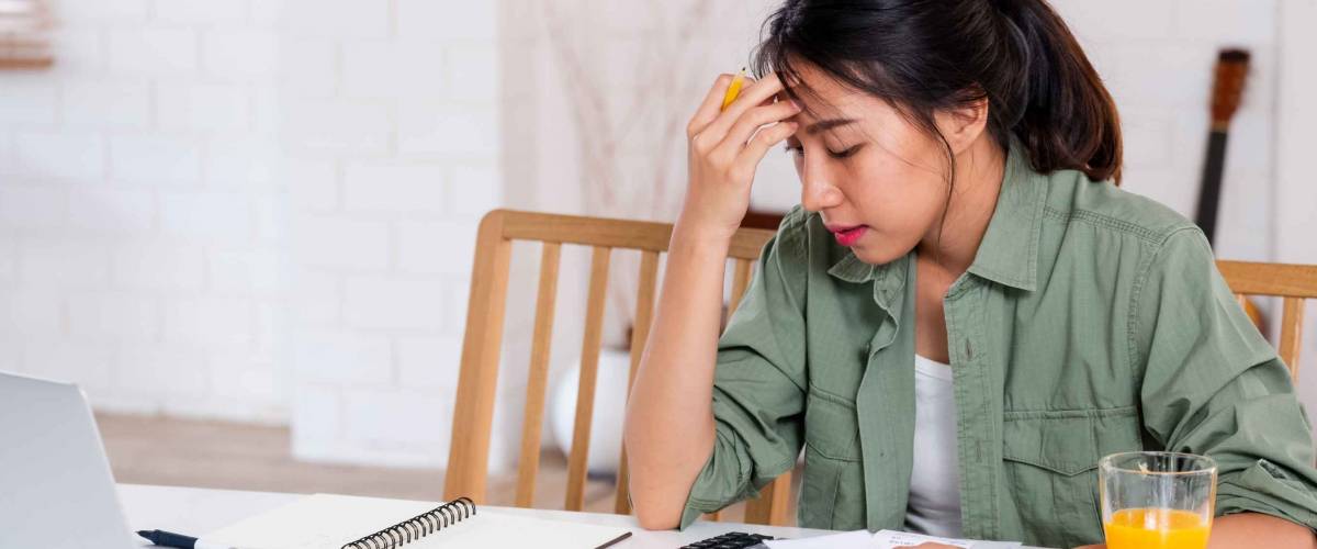 Stressed young woman sitting at kitchen table, looking at bills