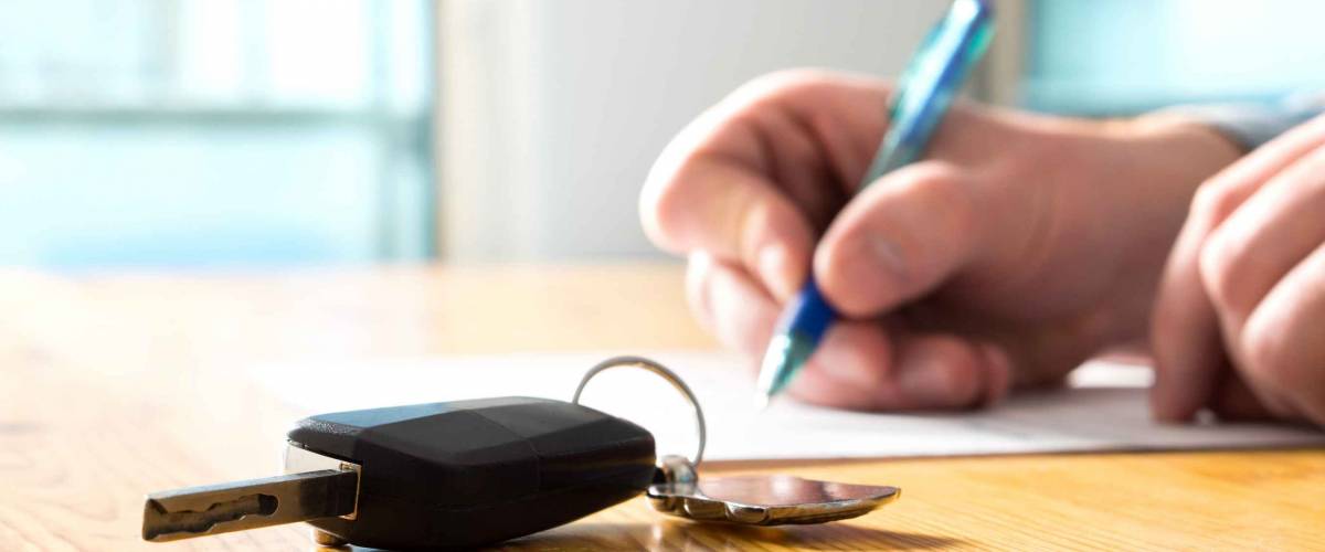 Close up of man signing paper on table with car keys in foreground