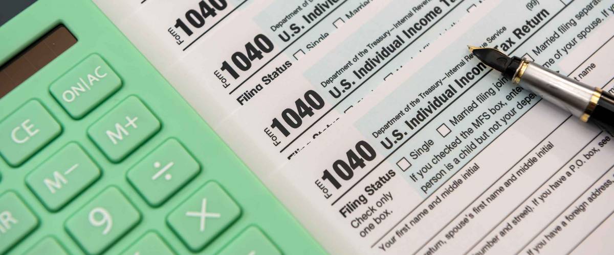 Pile of tax forms with green calculator beside it