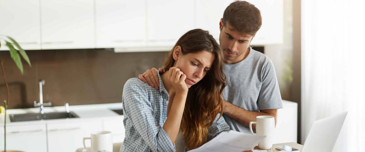 Young couple comforting each other in kitchen while looking at bills