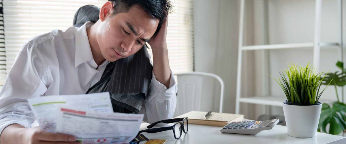 Stressed young asian businessman holding so many expenses bills such as electricity bill,water bill,internet bill,cell phone bill and credit card bill in his hand no money to pay debt