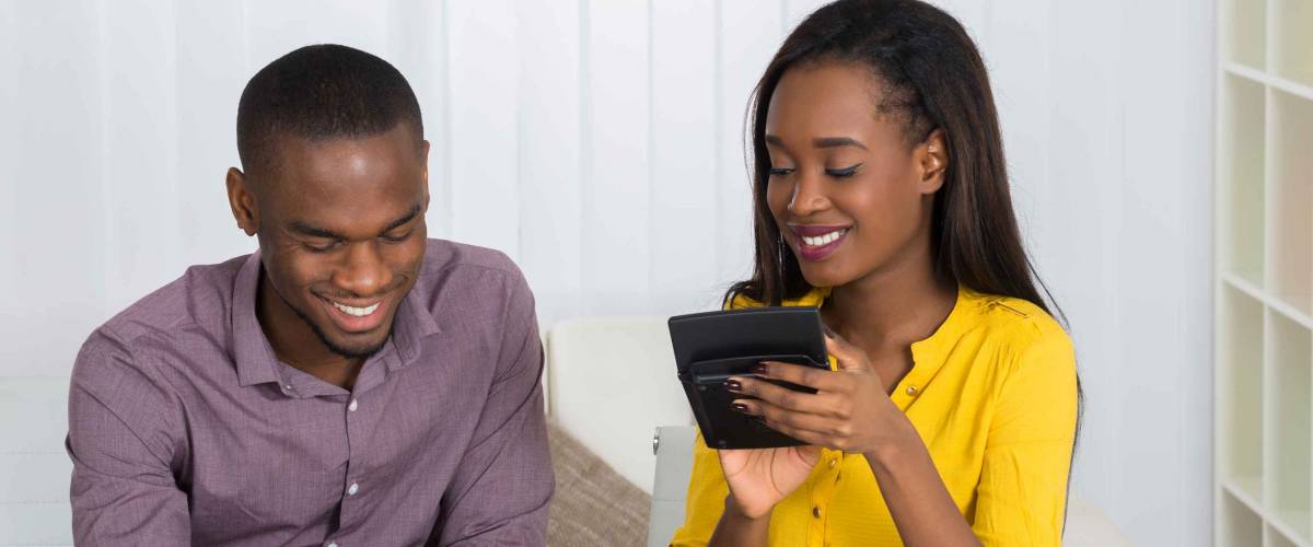 Happy Young Couple Calculating Bill With Coins And Piggybank On Desk