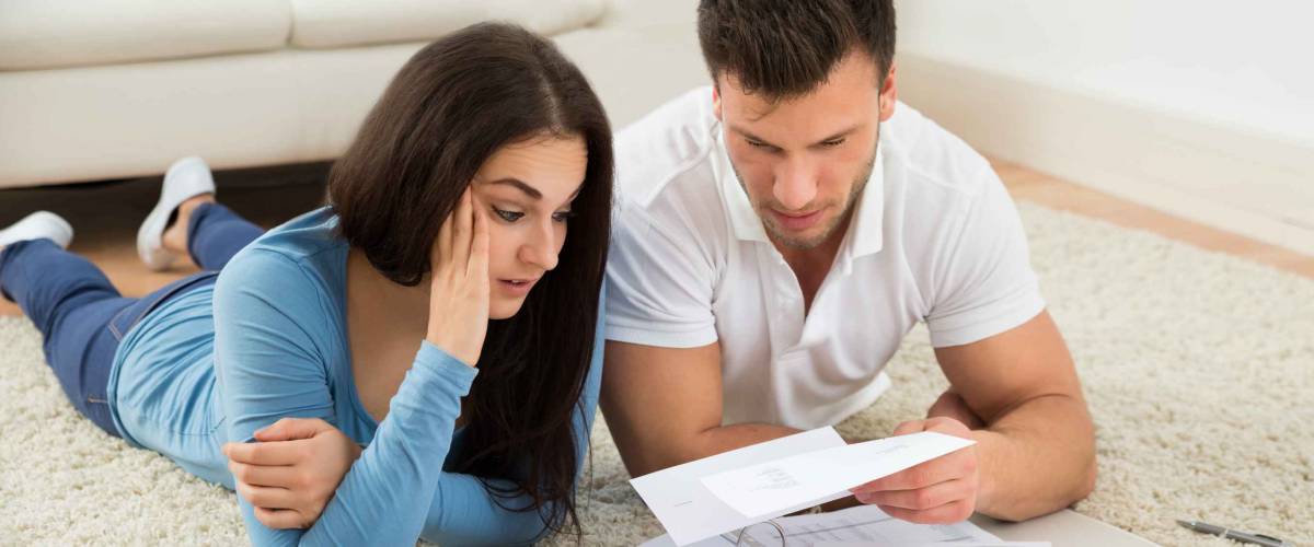 Worried Young Couple Lying On Carpet Calculating Their Bills At Home