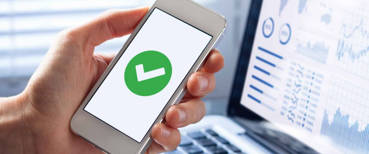 Hand holding a smartphone with a green checkmark icon on the screen to show a validated, confirmed, completed or approved status